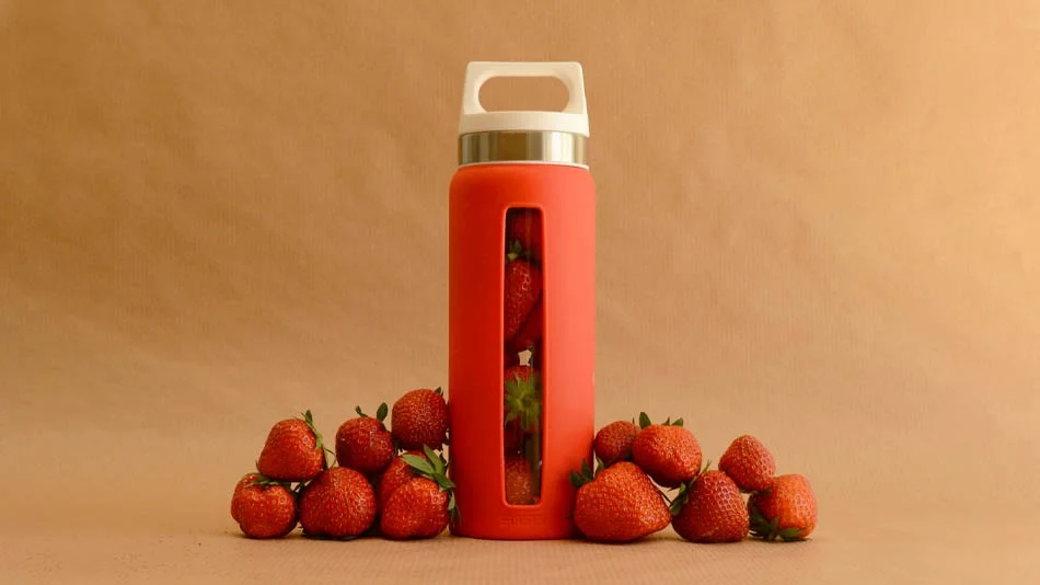 a red water bottle surrounded by strawberries