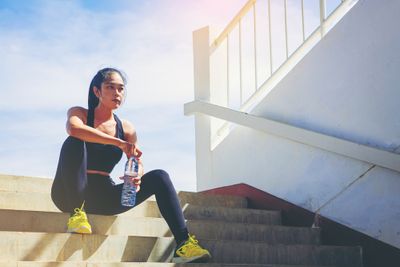 An athletic woman sitting on the stairs holding a bottle of electrolyte-enriched water for a post-workout energy boost