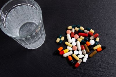 Various tablets and capsules on a black background next to a glass of water