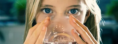 Lady drinking water from a glass, looking directly at the camera
