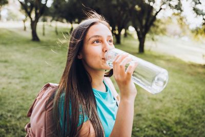 A woman drinking water from a glass bottle.