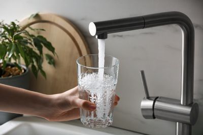 A person holding a glass of water in front of a faucet.