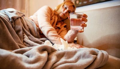 A sick woman in bed with a glass of water to hydrate.
