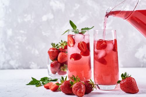 A pitcher of liquid pouring into a glass filled with strawberries