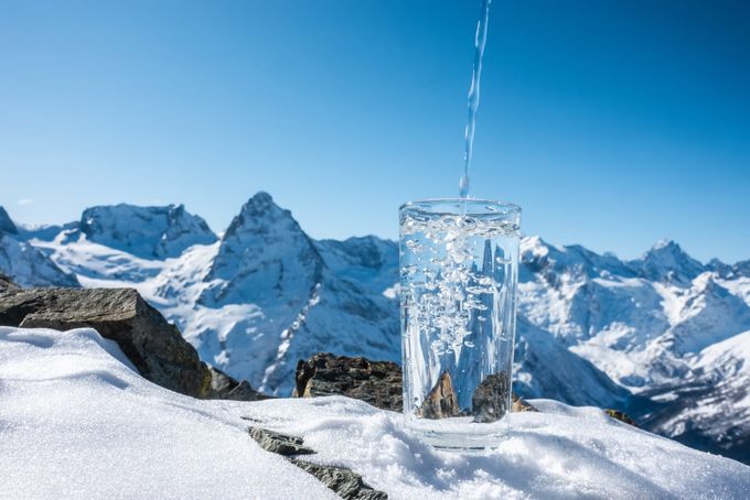 Pure cold water being poured into a glass with a backdrop of snowy mountains