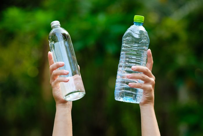 Person holding a glass bottle in one hand and plastic bottle in another