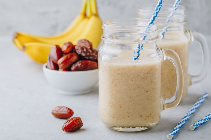 Banana and date fruit smoothie or milkshake in glass mason jar on a grey stone background