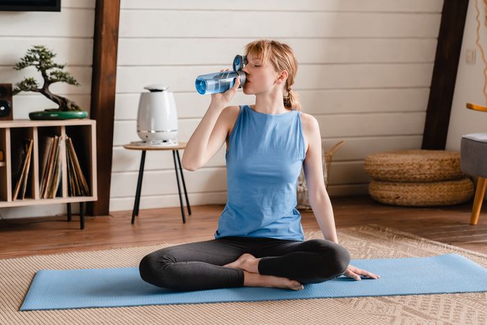 Woman sitting on a yoga mat drinking water from a blue glass bottle