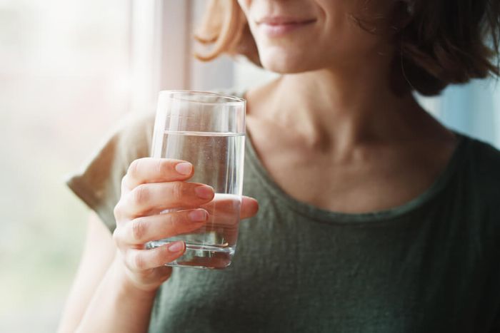 A woman holding a glass of water to drink in her hand.