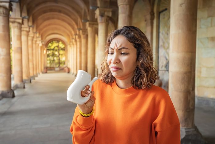 Woman standing in hallway with concrete pillars looking disgusted by ceramic jug