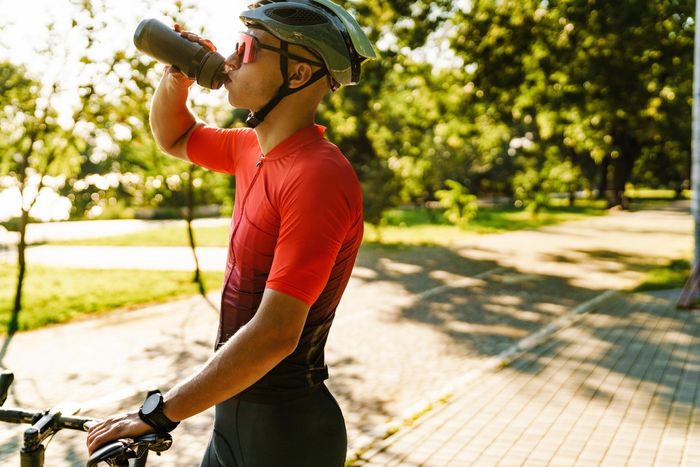 A man in a helmet drinking from a water bottle.